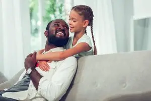 A father looks lovingly at a daughter giving him a hug.