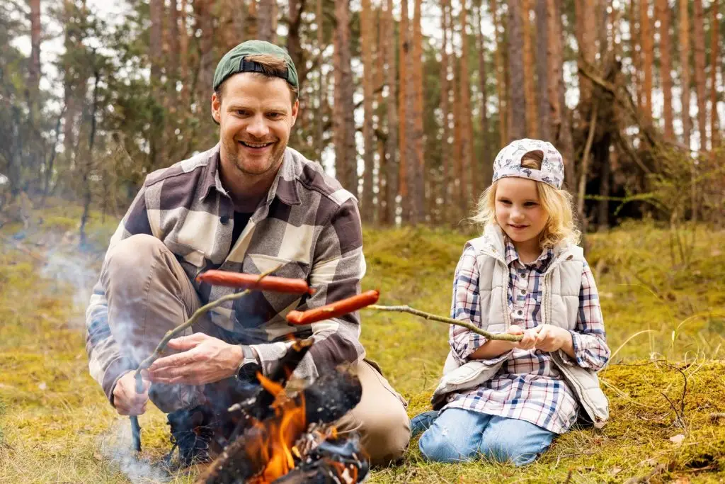 Father and daughter roasting a hotdog over a fire.