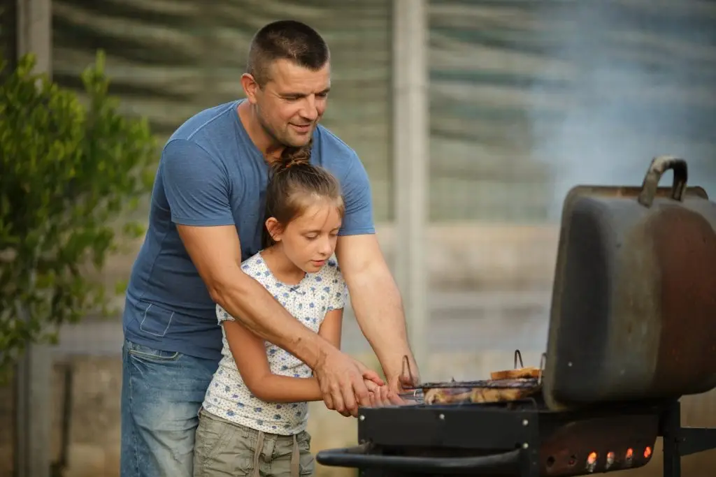 Photo of a father teaching a daughter to grill.
