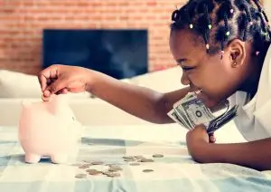 Girl putting money in piggy bank.